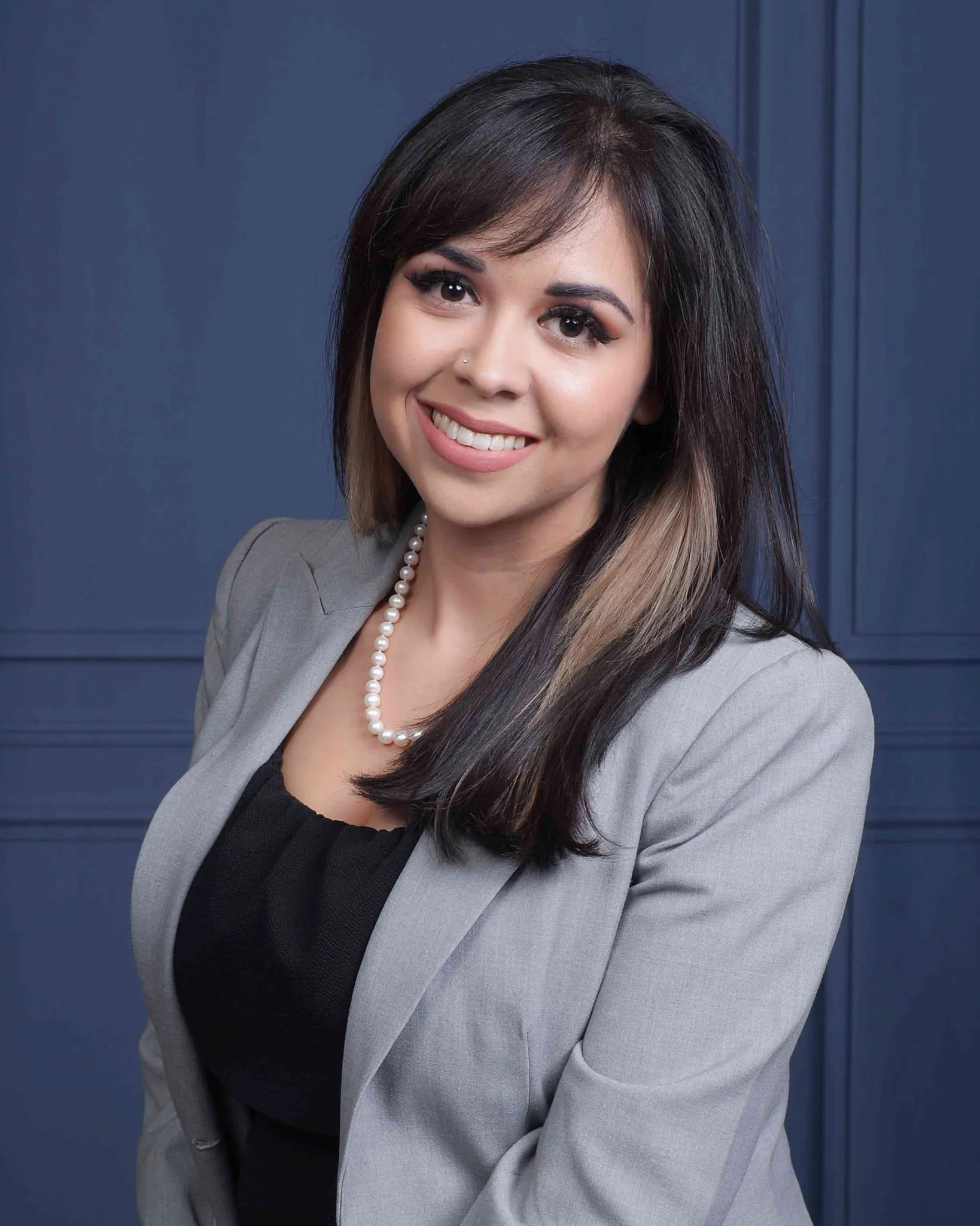 Gina Quintanilla smiling, in a grey blazer and pearl necklace